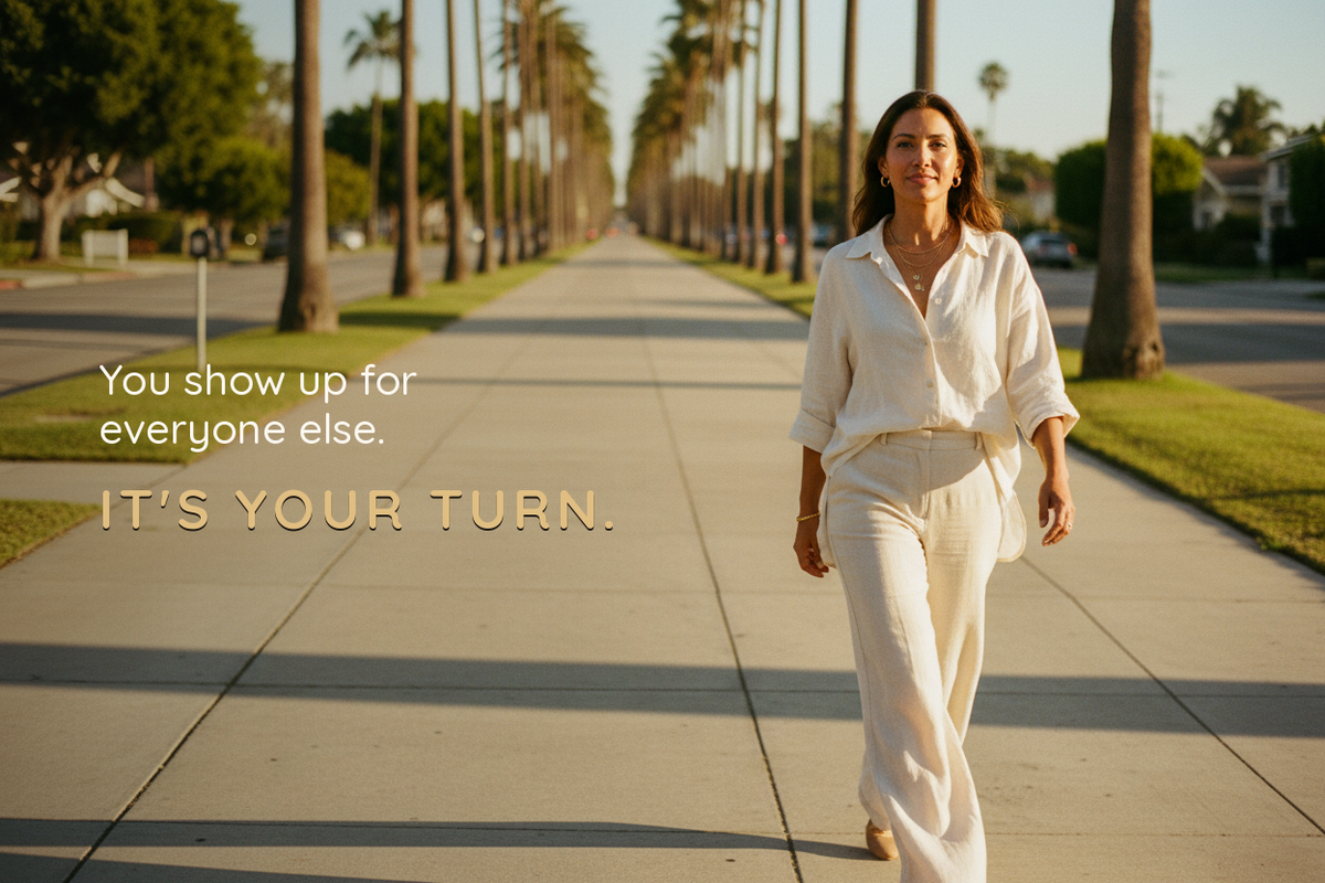 Woman in white linen walking down a palm-lined sidewalk at golden hour. Text reads: You show up for everyone else. It's your turn.